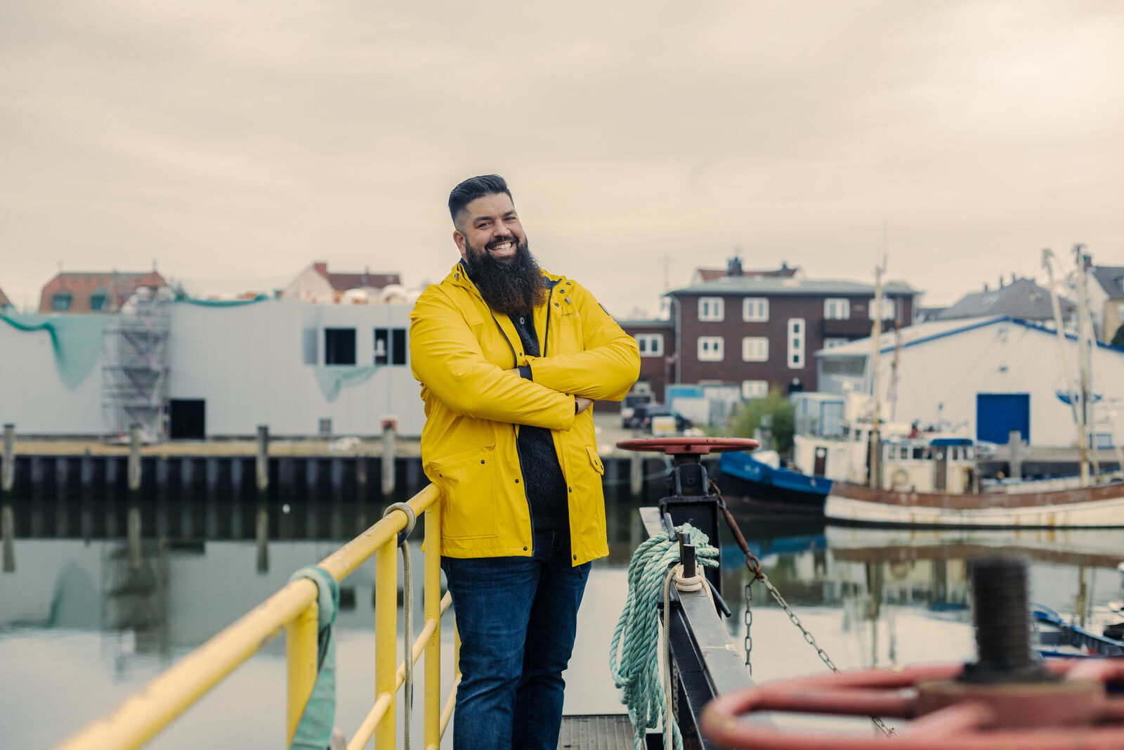 Thorsten Schwarz in gelber Regenjacke, an eine Hafenreling gelehnt, im Hintergrund ein norddeutscher Hafen